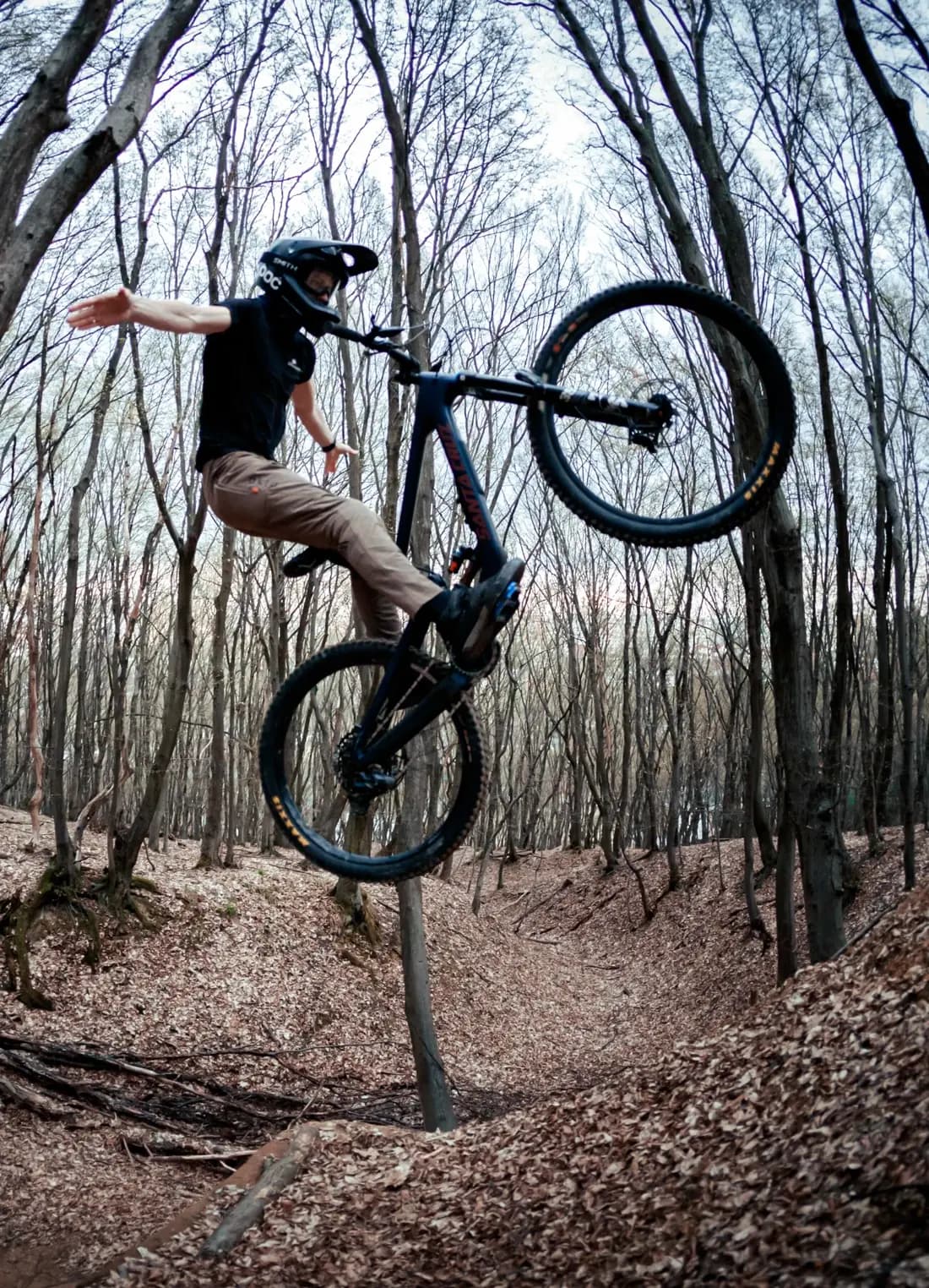 Ivan Krzák doing a tailwhip on his mountain bike over a forest trail jump
